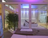 Un'oasi talassoterapico a Rimini, con due persone che si rilassano su lettini in un ambiente moderno e luminoso, circondato da piante di bambù e illuminazione soffusa.