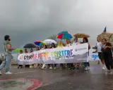 Persone con ombrelli colorati sfilano a Rimini Pride, tenendo uno striscione arcobaleno con scritto "Esistere Mere Esistere".