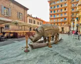 Statua di rinoceronte in una barca, in una piazza di Rimini, dove è nato Fellini. Tavolini all'aperto e palazzi colorati sullo sfondo.