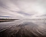 Spiaggia deserta con onde che lambiscono la riva, tre bandierine piantate nella sabbia bagnata. Un'atmosfera malinconica per questo mare d'inverno.