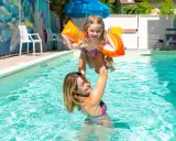 Mamma solleva la figlia con braccioli arancioni in una piscina, un momento di gioia in un bagno giardino a Cesenatico.