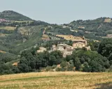 Borgo collinare di **Cerreto di Saludecio** con case in pietra e una chiesa, immerso nel verde della campagna romagnola.