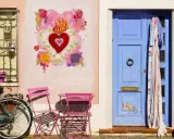 Un angolo pittoresco di Borgo San Giuliano a Rimini: una porta blu, un cuore fiammeggiante dipinto, una bicicletta e sedie rosa.