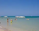 Persone si godono una giornata di sole sulla spiaggia libera di Torre Pedrera, tra bagni e relax in mare.