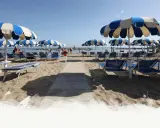 Ombrelloni a righe blu e bianche e lettini preparati per i visitatori al Delfini Beach Village Cattolica, con il mare sullo sfondo.
