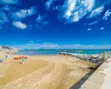 Spiaggia di Bellaria Mare con lettini, bagnini arancioni e mare azzurro sotto un cielo blu con nuvole bianche.