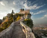 Sentiero in pietra che sale verso le fortificazioni di San Marino città, con vista panoramica sulla valle sottostante.