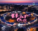 Un vivace evento serale a Rimini Comix, con bancarelle illuminate, una ruota panoramica e il logo rosa che domina la scena.