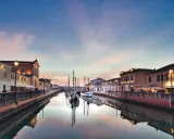 Canale di Cesenatico al tramonto, con barche a vela ormeggiate e riflessi sull'acqua. La riviera cesenatico incanta con i suoi colori.