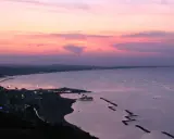 Panoramica Gabicce al tramonto, con cielo rosa e viola, mare calmo e costa illuminata.