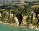 Scogliere a picco sul mare turchese a Gabicce Mare, Marche. Campi coltivati e vegetazione rigogliosa adornano le colline retrostanti.