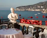Tavolo apparecchiato con vista mare, perfetto per idee per Ferragosto. Busto in marmo, fiori rossi e panorama mozzafiato.