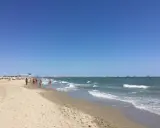Spiaggia affollata a Ravenna, con gente che passeggia sulla sabbia e nel mare. All'orizzonte, barche e un cielo azzurro intenso.