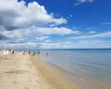 Una giornata di sole a Riccione mare, con gente che passeggia sulla sabbia e si gode l'acqua cristallina sotto un cielo azzurro con nuvole bianche.