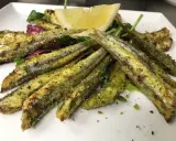 Sardoncini alla romagnola dorati e croccanti, serviti su un letto di insalata fresca con una fetta di limone.