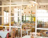 Interno di un'osteria de borg con tavoli apparecchiati con tovaglie a quadretti verdi e bianchi, sedie in legno e decorazioni colorate.