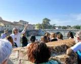 Guida turistica con gruppo a Rimini, che ascolta storie sui **eventi rimini** e la storia locale, con un ponte antico sullo sfondo.