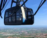 Cabina della funivia di San Marino in primo piano, con vista panoramica sulla città e sul mare all'orizzonte.