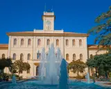 Fontana zampillante nella piazza Roosevelt di Cattolica, con un edificio giallo e un cielo azzurro.