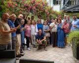 Un gruppo di persone sorridenti festeggia la primavera viserba sotto un pergolato fiorito.
