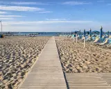 Passerella in legno sulla sabbia dorata di Rimini, con file di lettini e ombrelloni blu pronti per accogliere i bagnanti.