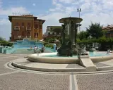 Fontana con statue e tartarughe in una piazza di Cattolica centro, con edifici storici e persone che si godono il sole.