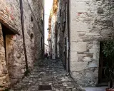 Un vicolo acciottolato a Pennabilli, Rimini, con antiche case in pietra e una persona con un cappotto rosa.