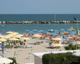 Spiaggia affollata con ombrelloni gialli e bianchi, lettini e il mare azzurro. Un'immagine di igea marittima, perfetta per una vacanza.