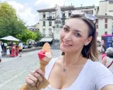 Una donna sorride tenendo un cono gelato, con una piazza e un monumento sullo sfondo. Un assaggio di gelato che ricorda la gelateria Gabicce Mare.