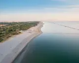 Vasta spiaggia dorata e mare calmo, con file di ombrelloni che delineano un lido di classe. All'orizzonte, la costa punteggiata di verde e costruzioni.