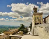 Torre del Campanone e Palazzo Pubblico nel **San Marino centro**, con vista panoramica sulle colline verdi sotto un cielo azzurro e nuvoloso.