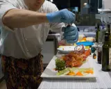 Chef con guanti blu macina pepe su un'aragosta, un piatto che sembra uscito da "lo zodiaco Rimini".