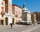 Passeggiata nella soleggiata piazza Tre Martiri a Rimini, con i suoi palazzi storici e il caratteristico orologio.