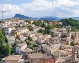 Panoramica di un borgo collinare con tetti rossi e una chiesa con campanile, incorniciato dal verde e dalle montagne. Un paesaggio che evoca la bellezza di Rimini e dintorni.