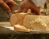 Mani esperte tagliano un pezzo di talamello formaggio di fossa, mostrando la sua consistenza rustica e invitante.