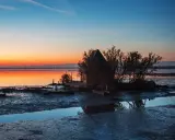 Tramonto sulla spiaggia di Marano, con una piccola capanna e un'imbarcazione riflessi sull'acqua calma.