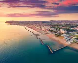 Alba rosata sul porto di Cattolica, con la costa e le spiagge dorate che si estendono verso l'orizzonte.