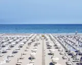 File di ombrelloni bianchi e lettini ordinati sui **stabilimenti balneari Cervia**, con il mare azzurro sullo sfondo.