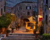 Antica scala a Gabicce Monte illuminata da lampioni, con un pozzo in mattoni e piante in vaso.