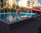 Piscina con scivolo rosso e giochi d'acqua ai Bagni Carmen Cattolica. Riflessi degli edifici nell'acqua azzurra.