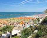 Spiaggia affollata a Gabicce Mare, con file infinite di ombrelloni colorati e lettini. Le recensioni la descrivono come un paradiso estivo.