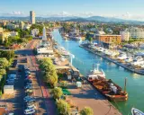 Vista aerea del porto di Rimini con barche ormeggiate, edifici e montagne sullo sfondo.