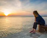 Donna seduta osserva il tramonto a Rimini, con il sole che si riflette sul mare calmo.
