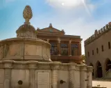 Fontana in pietra con pigna, edifici storici e cielo azzurro. Un assaggio dei monumenti di Rimini.