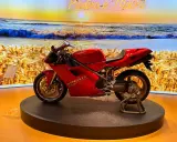 Ducati rossa su un palco, con sfondo di un campo di grano e il mare al tramonto. Un connubio perfetto tra la piada e il mare.