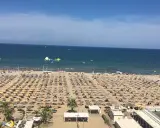 Una vasta spiaggia di Miramare gremita di ombrelloni e lettini, con bagnanti che si godono il sole e il mare azzurro.