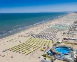 La riviera di Rimini in pieno sole, con un mare azzurro e una spiaggia affollatissima di ombrelloni colorati e bagnanti.
