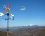 Gallo segnavento su sfondo azzurro, con montagne innevate all'orizzonte. Un invito a scoprire cosa vedere in Valmarecchia.