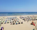 Spiaggia libera Viserba affollata di ombrelloni e lettini sotto un cielo azzurro. Bambini giocano nell'area attrezzata.
