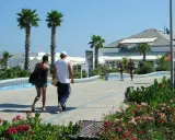 Coppia passeggia sul lungomare del parco mare nord Misano, tra palme e fiori.